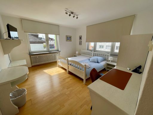 Helles Schlafzimmer mit Doppelbett, Schreibtisch und Fenster zur Straße.