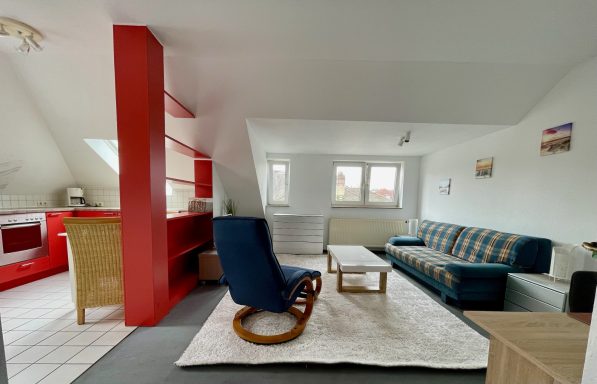 Helles Wohnzimmer mit roter Wand, blauer Relaxsessel und gemütlicher Couch.