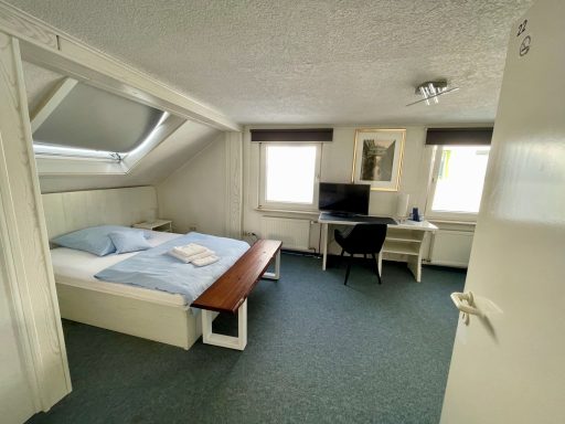 Helles Dachzimmer mit Doppelbett, Schreibtisch und Fernseher.