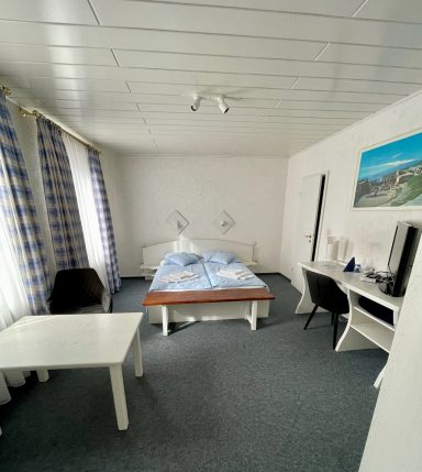 Helles, einfaches Zimmer mit einem Doppelbett, Tisch, Stuhl und Schreibtisch.
