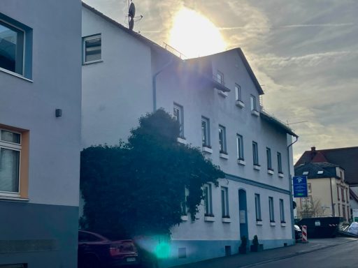 Helles Gebäude an einer Straße mit Sonne reflektiert und Schatten von einem Baum.
