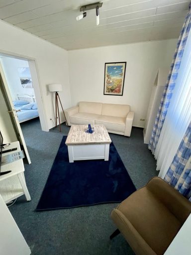 Heller Wohnraum mit Sofa, Tisch, Teppich und Blick auf einen weiteren Raum.