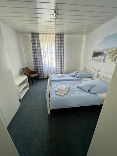 Helles Schlafzimmer mit zwei Betten, Stuhl und Fenster mit Vorhängen.