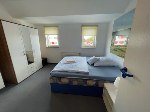 Helles Schlafzimmer mit Doppelbett, Kleiderschrank und Fenster.