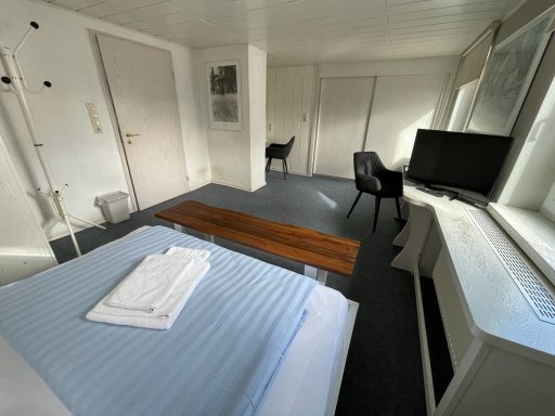 Helle Hotelzimmer mit Bett, Fernseher und Stühlen.