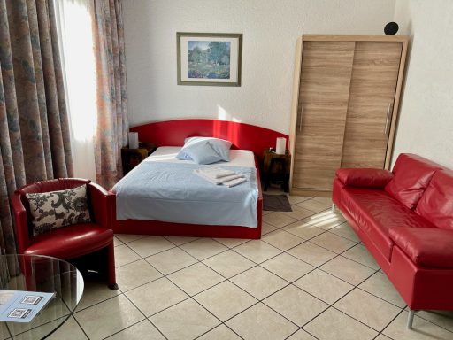 Rotes Schlafzimmer mit Bett, Sofa und Stuhl, helle Wände und Fenster.