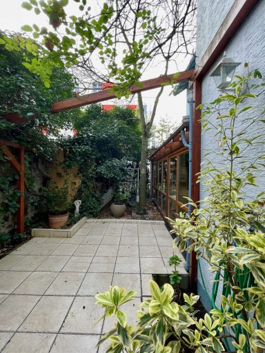 Pflasterfläche im Garten mit Grünpflanzen und einem Baum, umgeben von Wänden.