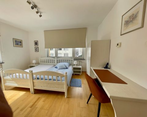 Helles Schlafzimmer mit einem Bett, Schreibtisch und Fenster, moderner und einladender Stil.