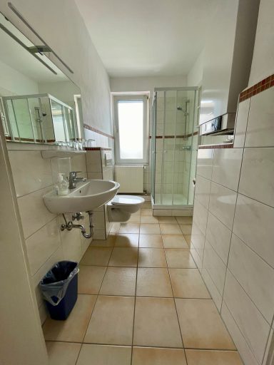 Heller Badezimmer mit Dusche, Waschbecken und WC, gefliest und mit großen Wandspiegeln.