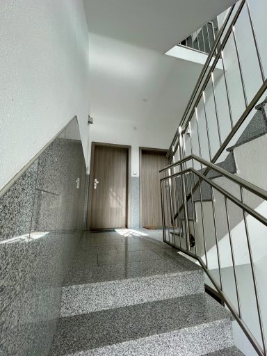 Treppenhaus mit grauem Boden, Geländer und zwei Türen am Ende des Flurs.