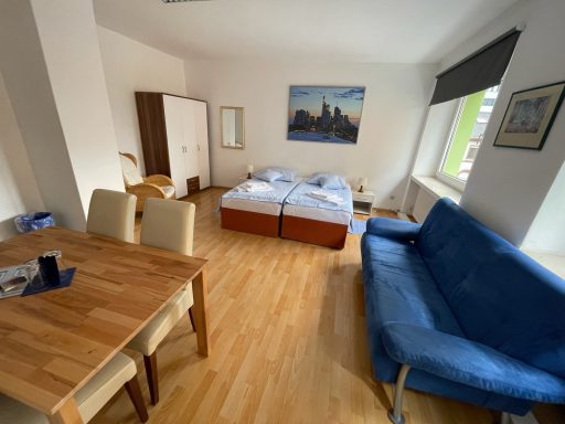 Helles Zimmer mit Doppelbett, Essbereich und blauem Sofa.