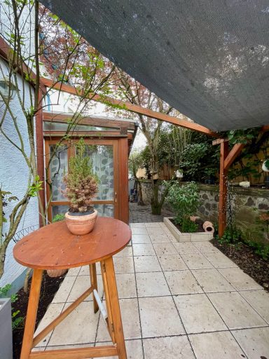 Ein gemütlicher Außenbereich mit einem Tisch, Topfpflanze und begrüntem Garten.