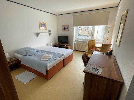 Helles Hotelzimmer mit zwei Betten, Fernseher, Schreibtisch und Fenster.