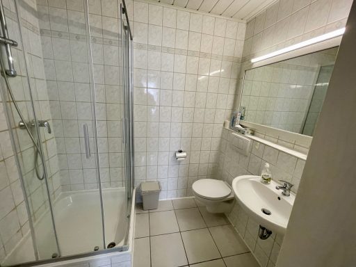 Modernes Badezimmer mit Dusche, Toilette und Waschbecken. Helle Fliesen und Spiegel.